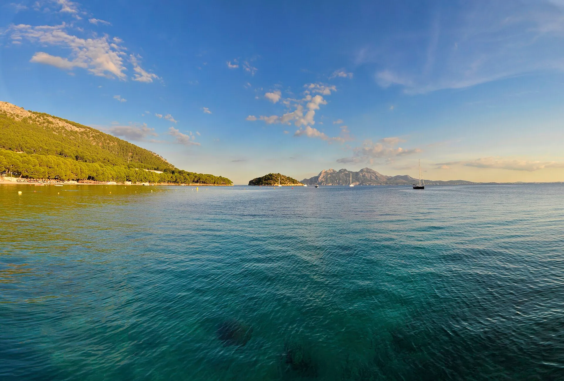 Turquoise water of the Badia de Pollença off the Formentor road, boats anchored under a clear sky.